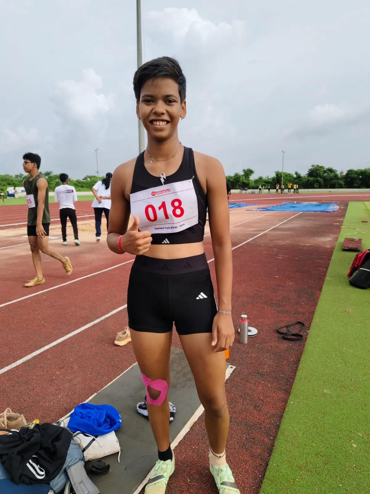 Female sprinter standing on running track with bib number 018